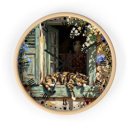 Round wall clock with a light wood frame and a printed illustration of a sleeping torte cat on a weathered blue-green window sill, surrounded by flowers and shutters.