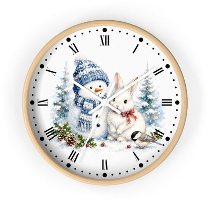 A round wall clock with a light wood frame and a white face featuring a winter illustration of a snowman in a blue hat and scarf, a white rabbit with a red bow, snowy trees, pinecones, and a small bird. The clock has black Roman numerals and black dot hour markers with white hands.