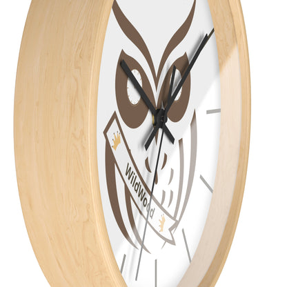 A close-up of a round wall clock with a light natural wood frame, a white dial, and a brown owl graphic holding a banner that reads 'WildWild'.