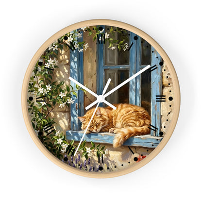 Round wall clock with a light wood frame and a printed illustration of an orange tabby cat sleeping on a blue window sill, surrounded by climbing white flowers and green leaves. The clock face has black Roman numerals and white clock hands, shown against a plain white background.