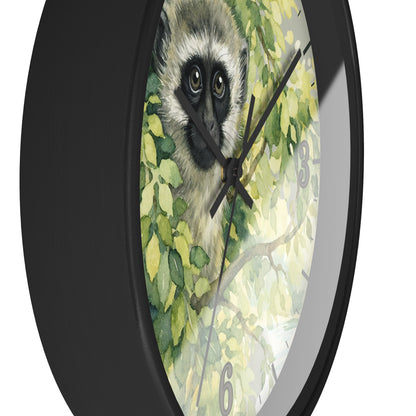 A round wall clock with a black frame and a printed face featuring a vervet monkey among green leaves, shown against a plain white background.