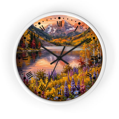 A round wall clock with a white frame and a scenic autumn landscape printed on the face, featuring a mountain, lake, colorful trees, and wildflowers. The clock has black Roman numerals and black hands on a plain white background.