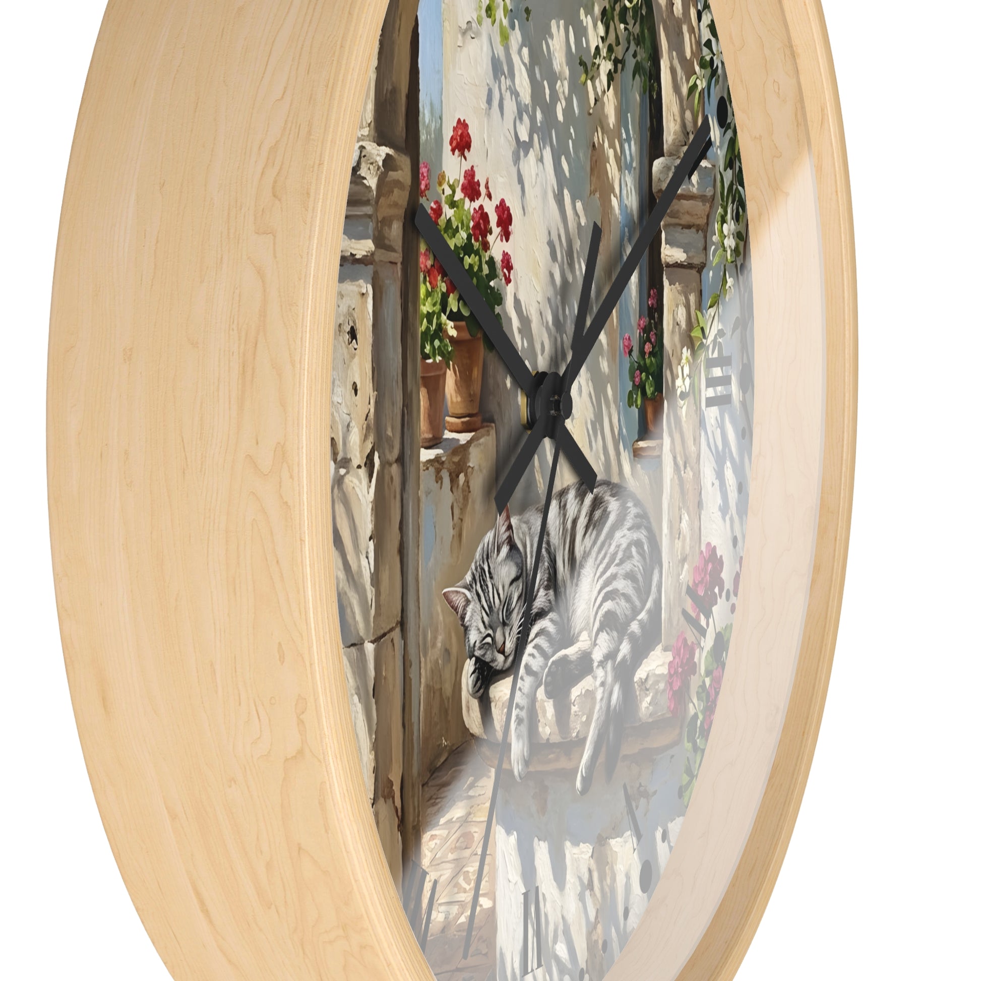 Round wall clock with a light natural wood frame and a printed center scene showing a gray tabby cat lounging on a windowsill with red flowers and outdoor shadows, photographed on a white background.