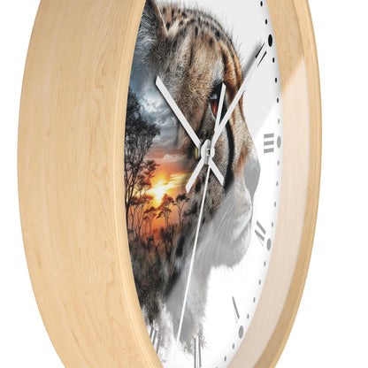 A round wall clock with a light natural wood frame and a white face featuring a split design: one half shows a cheetah face, the other half shows an African savanna sunset scene. The clock has white hands and black Roman numerals.