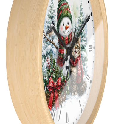 A round wall clock with a light natural wood frame and a white face featuring a winter holiday illustration of a snowman, a cat, evergreen trees, and red bows.