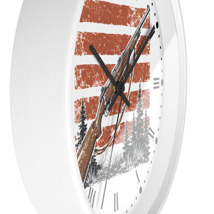 A white round wall clock with a rustic design featuring a rifle, pine trees, and distressed orange and white horizontal stripes on the face.