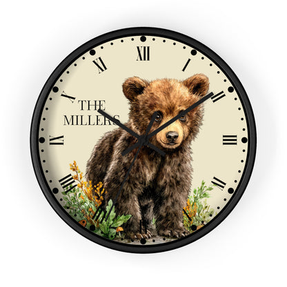A round wall clock with a black frame and a cream-colored face featuring an illustration of a brown bear cub, with the text 'THE MILLERS' on the left side. The clock is shown against a plain white background.