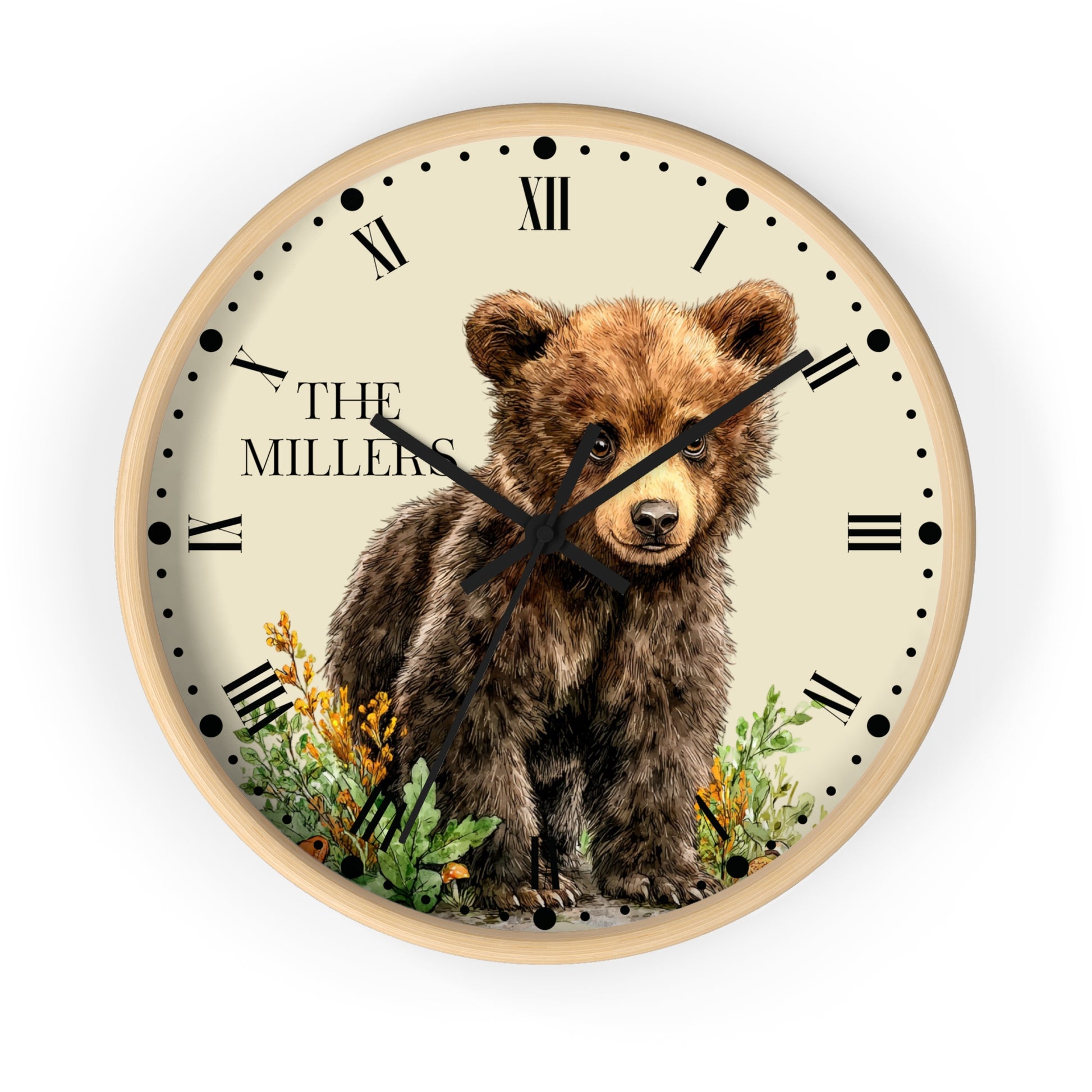 A round wall clock with a light wood frame and a cream-colored face, featuring an illustration of a brown bear cub standing among green plants and yellow flowers. The text 'THE MILLERS' is printed on the left side of the clock face, which is shown against a plain white background.