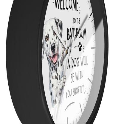 A round wall clock with a black frame and a white face featuring a Dalmatian illustration and the text 'WELCOME TO THE BATHROOM A DOG WILL BE WITH YOU SHORTLY'.