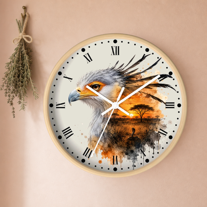 A round wall clock with a light wood frame, featuring a watercolor-style print of an eagle's head over an African savanna sunset scene. The clock is mounted on a warm beige wall next to a hanging sprig of dried herbs.