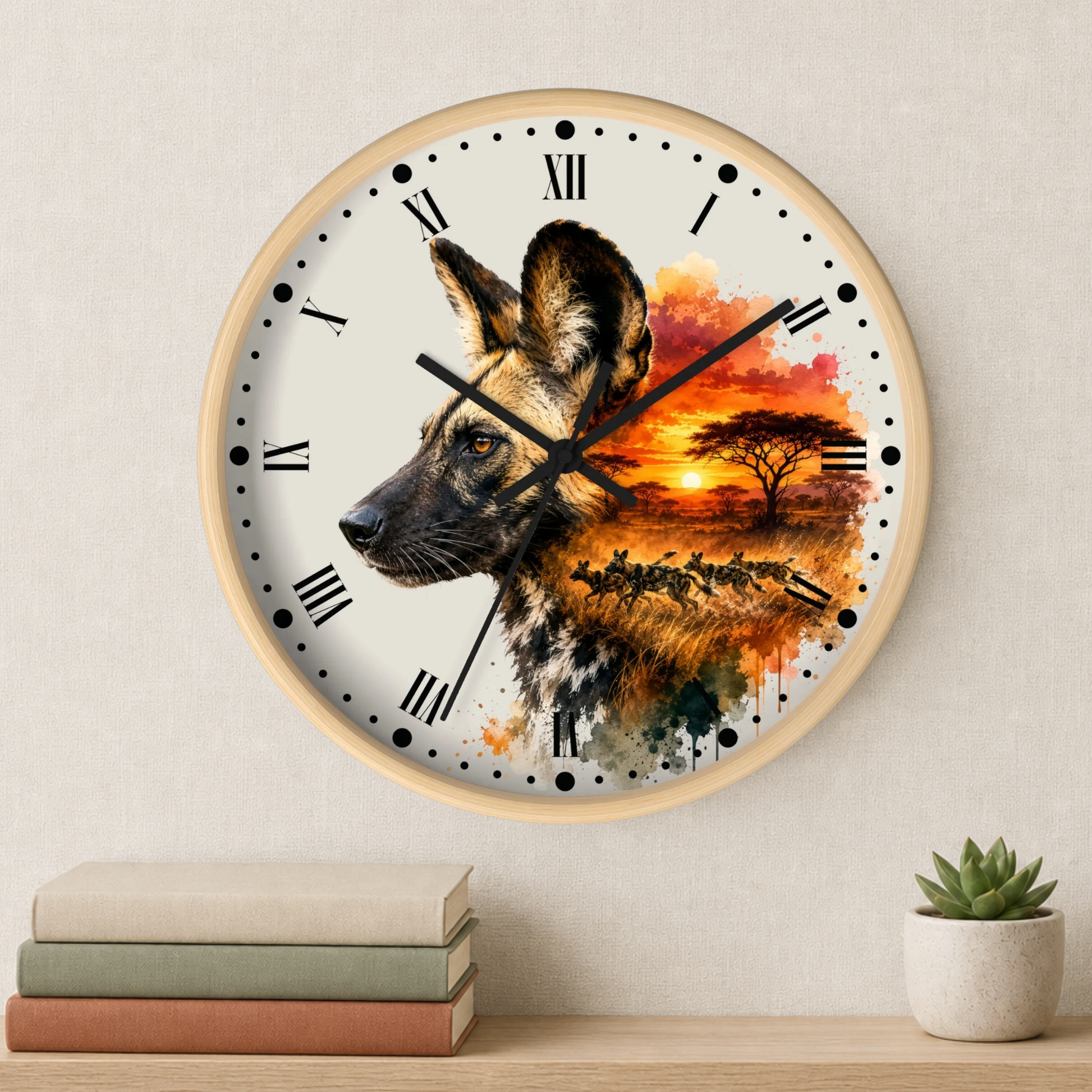 A round wall clock with a light wood frame and a printed design of an African wild dog in profile over a colorful savanna sunset scene. The clock is mounted on a light beige textured wall above a wooden shelf with stacked books and a small potted succulent.