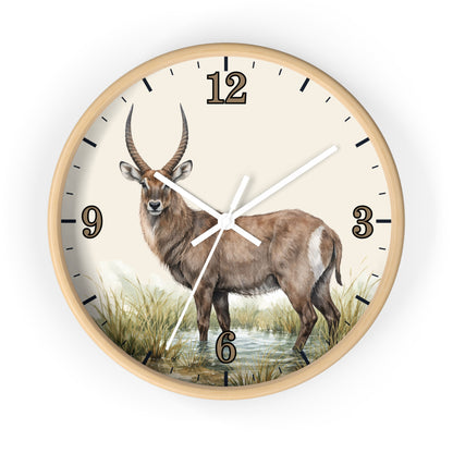 A round wall clock with a light wood frame and a cream-colored face featuring a detailed illustration of a waterbuck standing in grassy water. The clock has black Arabic numerals and white hands.