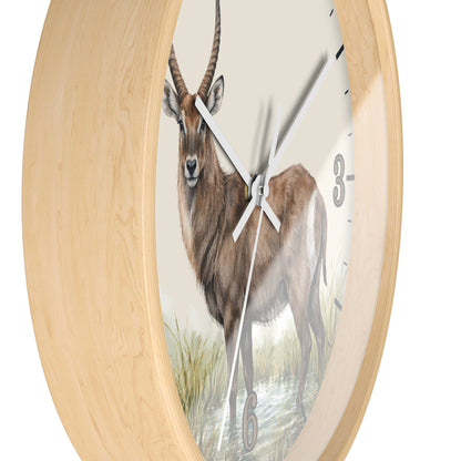 Round wall clock with a light natural wood frame and a printed illustration of a brown antelope standing in water, with white clock hands and partial black numerals visible.