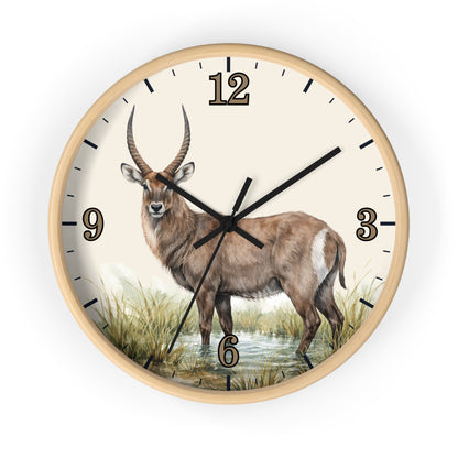 Round wall clock with a light wood frame and a cream-colored face featuring a detailed illustration of a waterbuck standing in grassy terrain. The clock has black hands, black hour markers, and a black outer rim, shown against a plain white background.