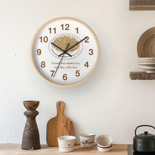 A round wall clock with a light wood frame and a white face, featuring a brain illustration at the center, black numerals, and the phrase 'Count the memories, not the calories' in brown script. The clock is mounted on a white wall above a wooden shelf with decorative items.