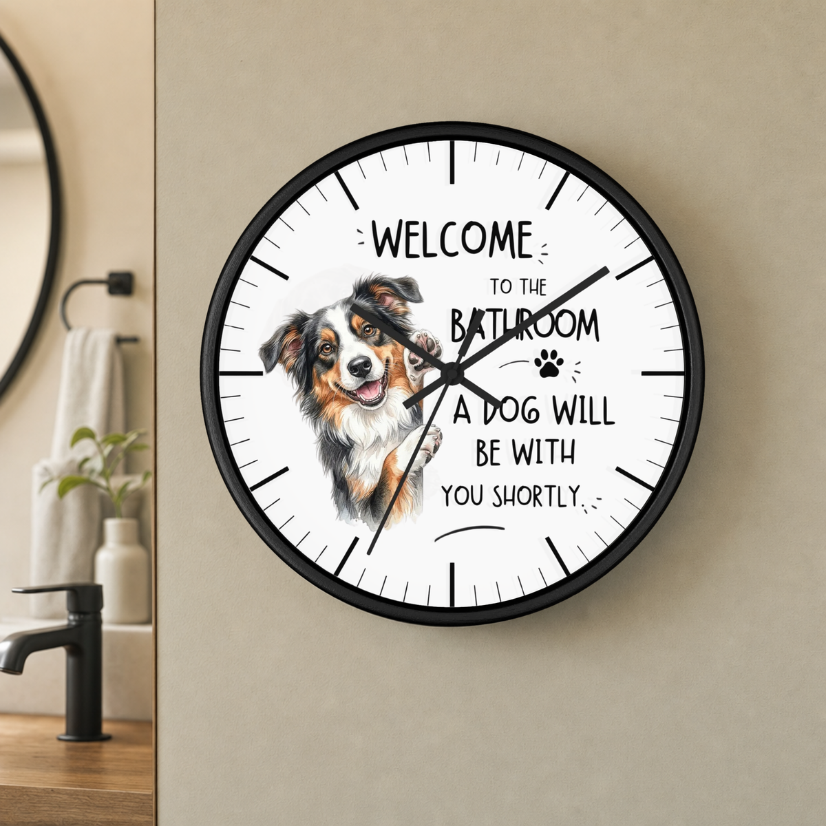 A round wall clock with a black frame and a white face, mounted on a beige wall in a bathroom setting. The clock features a painted Australian shepherd dog illustration and the text 'WELCOME TO THE BATHROOM A DOG WILL BE WITH YOU SHORTLY'.