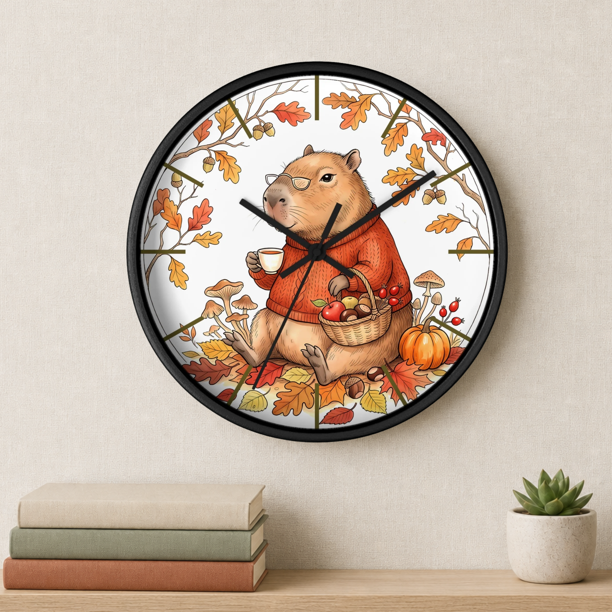 A round wall clock with a black frame and a whimsical autumn capybara illustration, hanging on a light beige wall above a shelf with books and a small succulent.