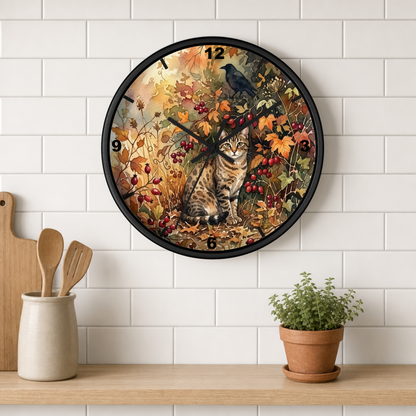 A round wall clock with a black frame hangs on a white subway-tile wall above a wooden shelf. The clock face features an autumn-themed illustration with a tabby cat, berries, leaves, and birds.