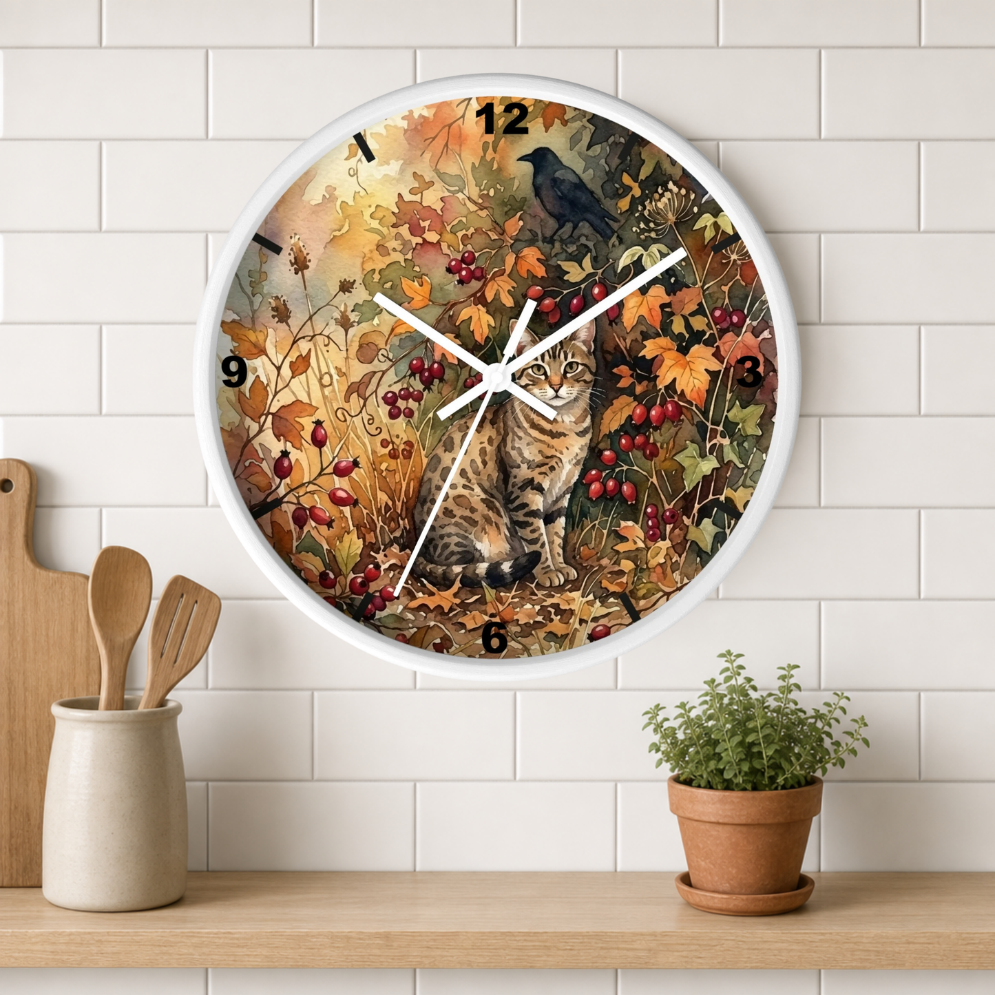 A round wall clock with a white frame hangs on a white subway-tile wall above a wooden shelf. The clock face features a detailed illustration of a tabby cat sitting among autumn leaves and red berries, with a black raven perched above.