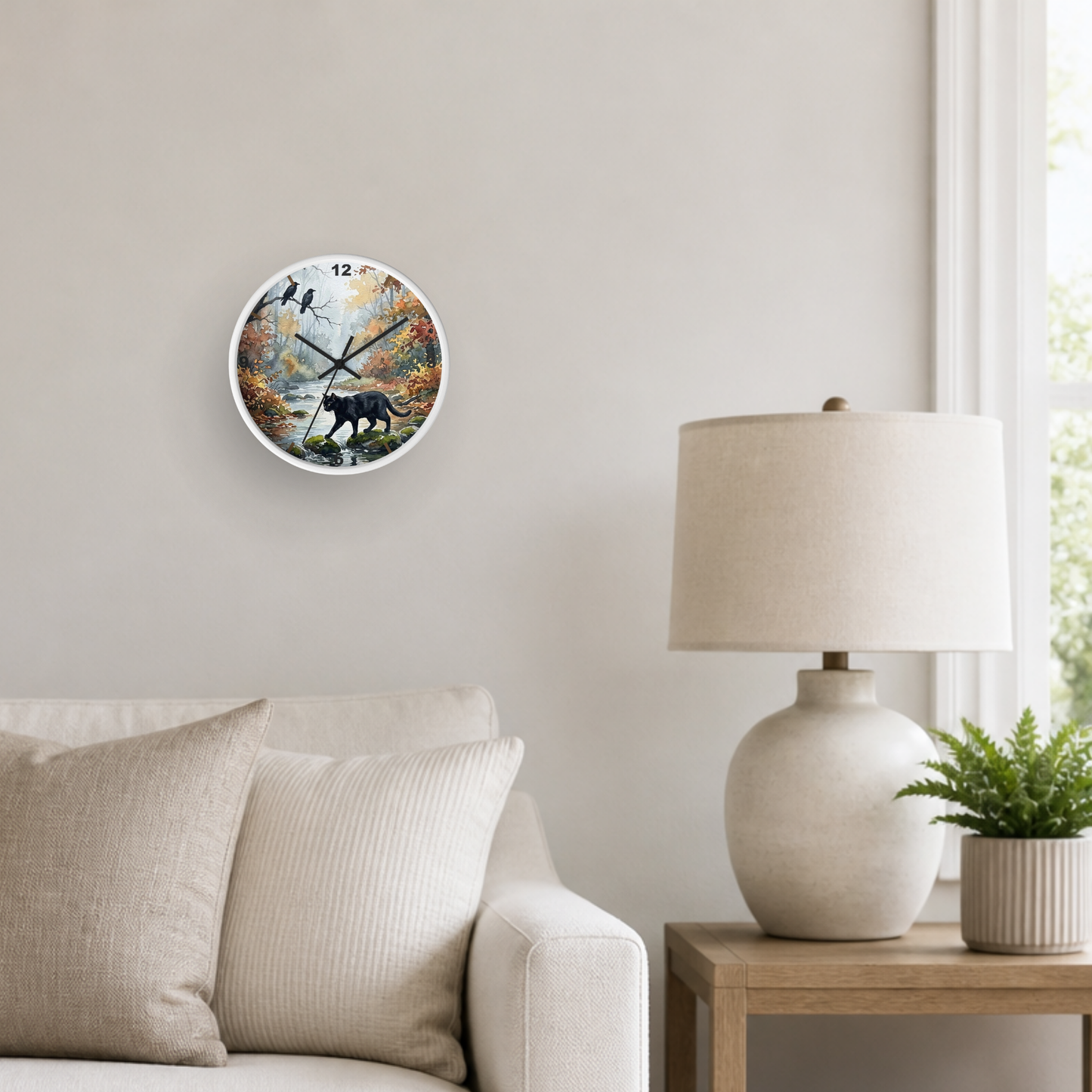 A round wall clock with a nature print of a black cat, birds, and autumn trees, styled on a beige wall in a living room setting next to a lamp and sofa.
