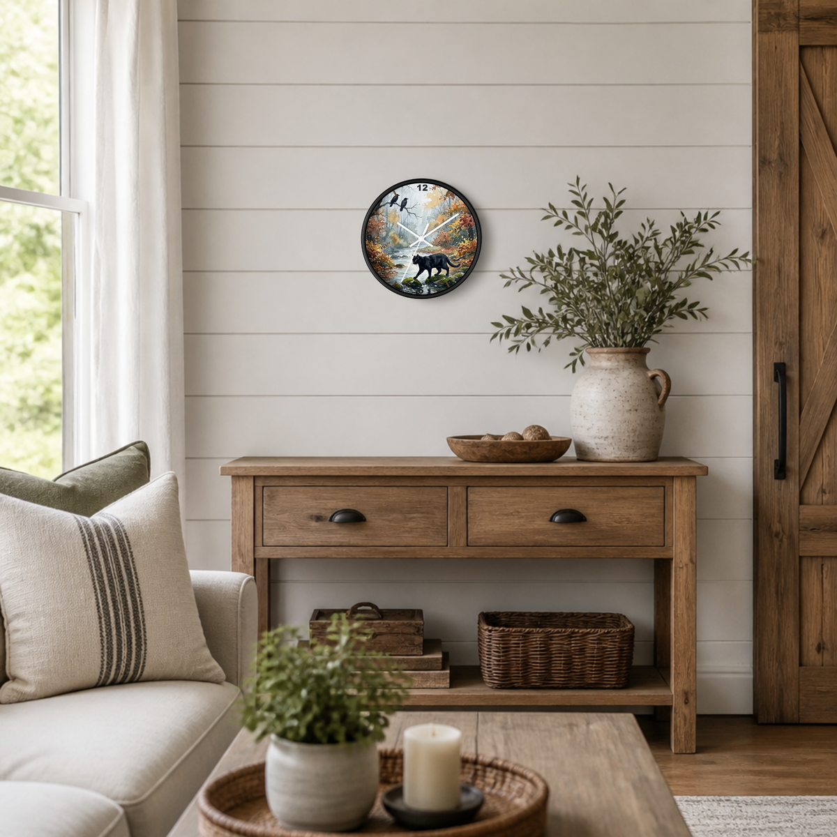 A round wall clock with a black frame and a rustic deer illustration, styled on a white shiplap wall above a wooden console table in a bright, modern farmhouse living room.