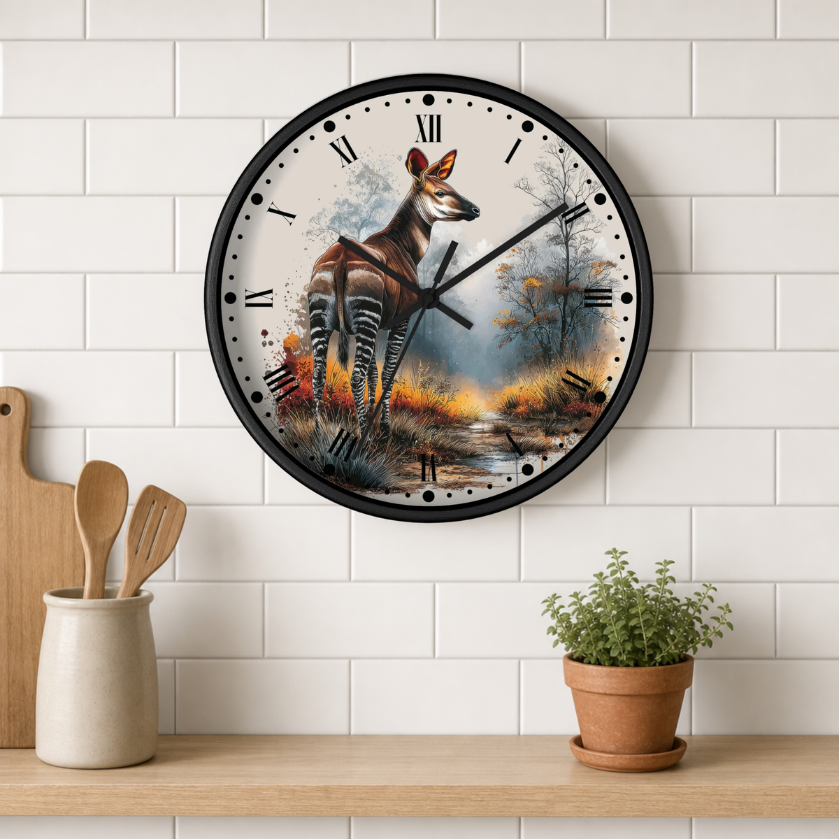 A round wall clock with a black frame hangs on a white subway tile wall above a wooden shelf. The clock face features a detailed painting of a zebra deer (Okapi antelope) standing in a misty forest at dusk.