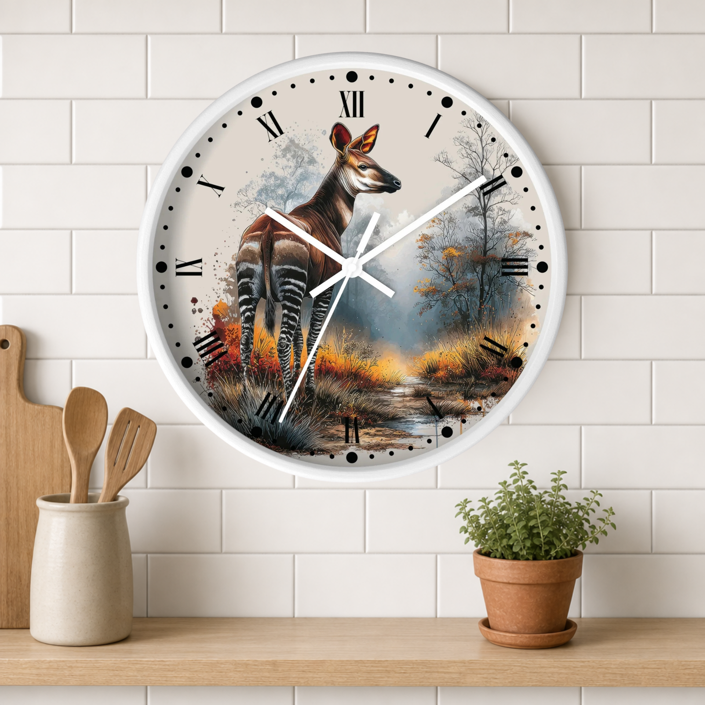 A round wall clock with a white frame and a printed scenic design featuring a zebra deer in a forest landscape, mounted on a white subway-tile wall above a wooden shelf with a small potted plant and utensils.