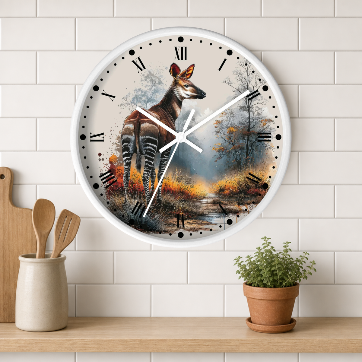 A round wall clock with a white frame and a printed scenic design featuring a zebra deer in a forest landscape, mounted on a white subway-tile wall above a wooden shelf with a small potted plant and utensils.