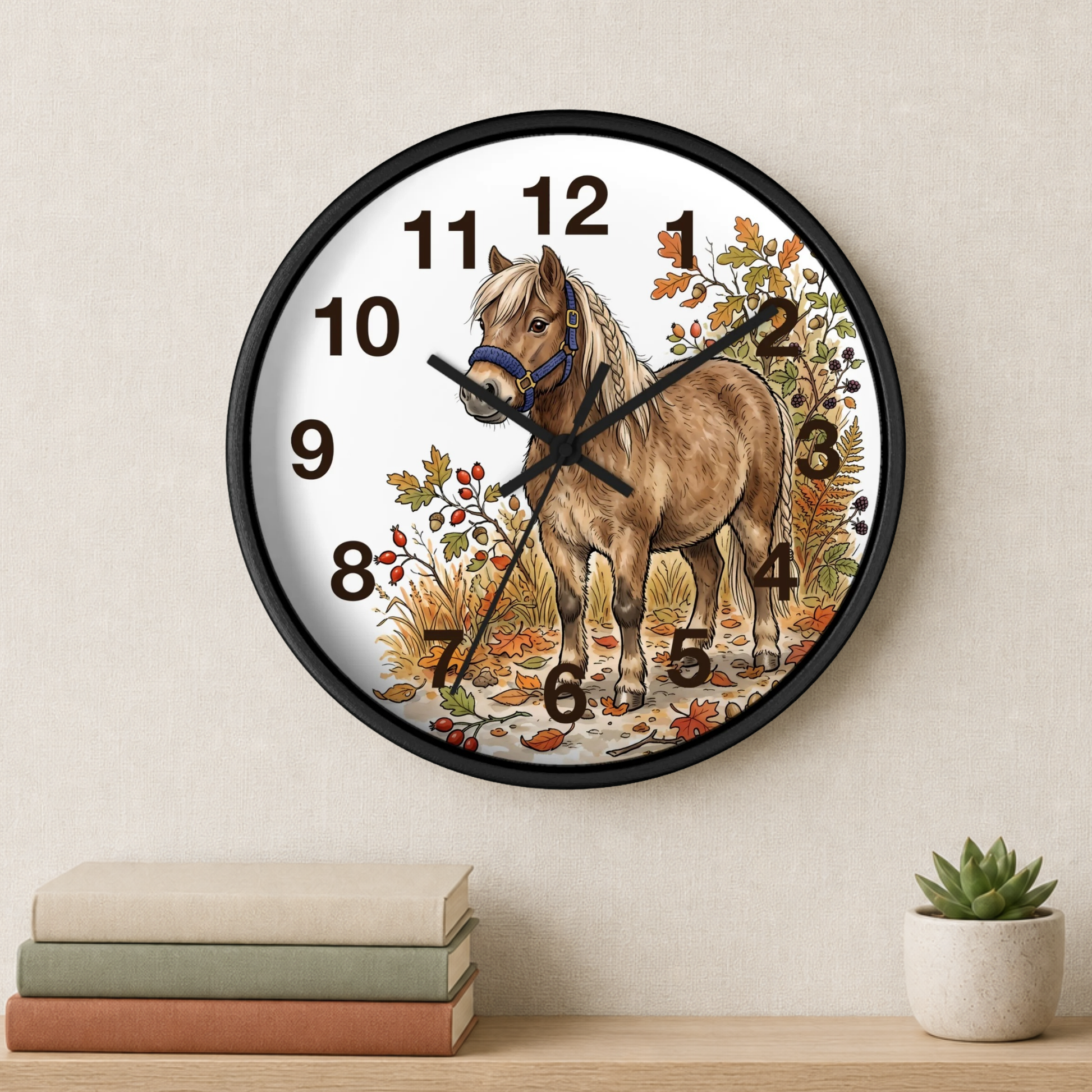 Round wall clock with a black frame and a white face featuring an illustration of a brown horse with autumn foliage. The clock is mounted on a beige wall above a shelf with books and a small potted succulent.