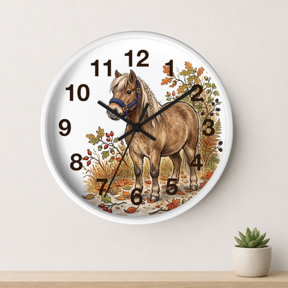 A round wall clock with a white face and frame, featuring an illustration of a light brown horse with autumn foliage and black Arabic numerals. The clock is mounted on a light beige wall above a wooden surface with a small potted succulent.