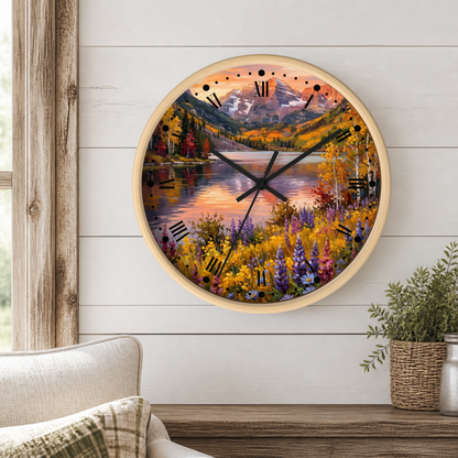Round wall clock with a scenic mountain lake landscape print, mounted on a white wood-paneled wall above a wooden table with a potted plant and part of a sofa visible.