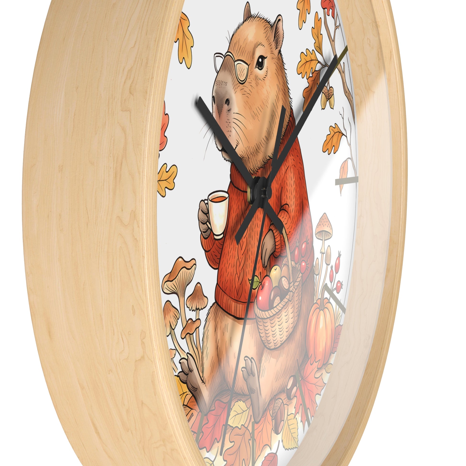 Round wall clock with a light natural wood frame and a whimsical illustration of a capybara wearing glasses and an orange sweater, holding a mug and a basket of autumn produce, on a white background.