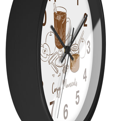 A close-up of a round wall clock with a black frame and a white face featuring brown coffee-themed illustrations, including a mug, a jar, and the words 'Cozy Moments'.