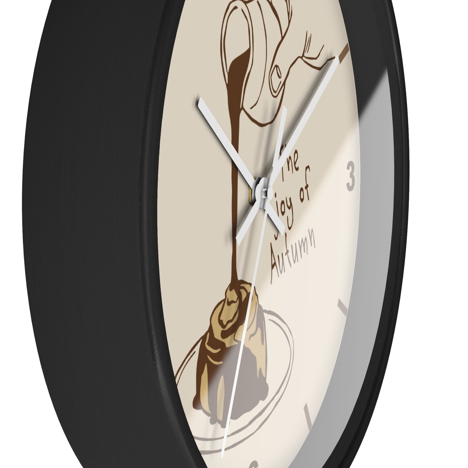 A close-up of a round wall clock with a black frame and a cream-colored face. The dial features an illustration of chocolate drizzled over a pastry, with the text 'the joy of Autumn' and partial black numerals.