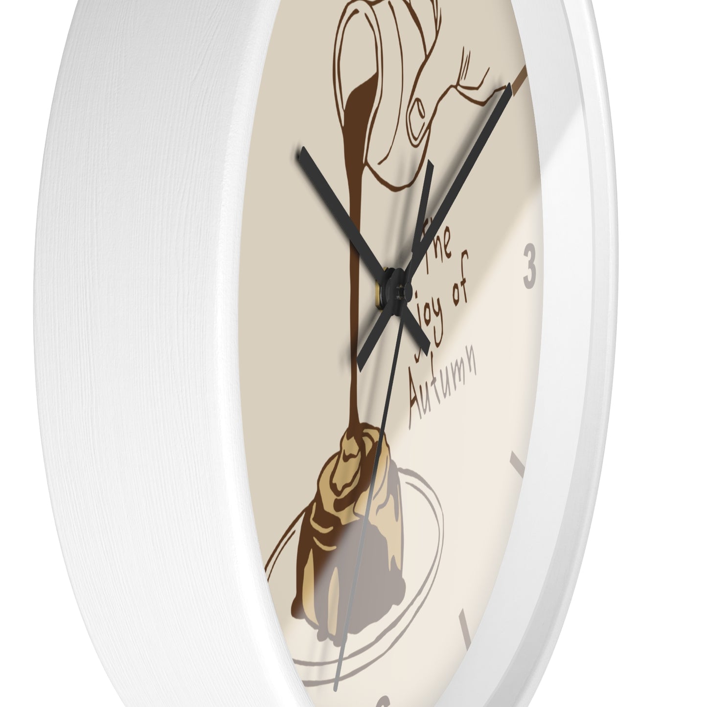 A close-up of a round wall clock with a white frame and a cream-colored face featuring an illustration of chocolate drizzle over a pastry and the words 'The Joy of Autumn'.
