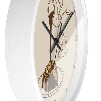 A close-up of a round wall clock with a white frame and a cream-colored face featuring an illustration of chocolate drizzle over a pastry and the words 'The Joy of Autumn'.