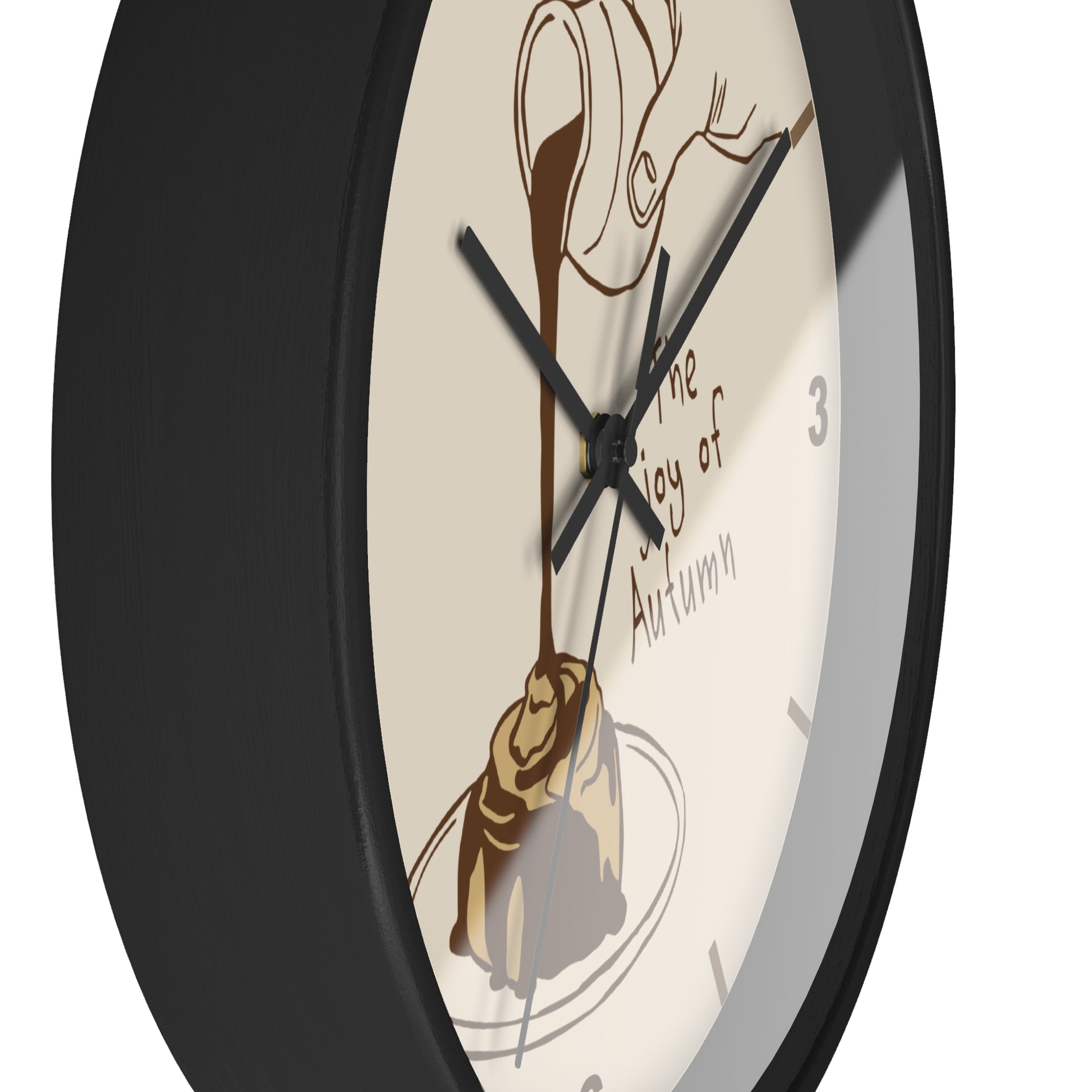 A close-up of a round wall clock with a black frame and a cream-colored face featuring an illustration of chocolate drizzle over a pastry and the text 'The Joy of Autumn'.