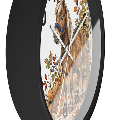 A round wall clock with a black frame and a printed illustration of a brown horse with a blue halter among autumn leaves on the dial.