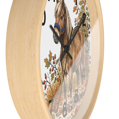 Round wall clock with a light natural wood frame and a printed horse illustration on the face, featuring a brown horse with a blue halter and autumn foliage.