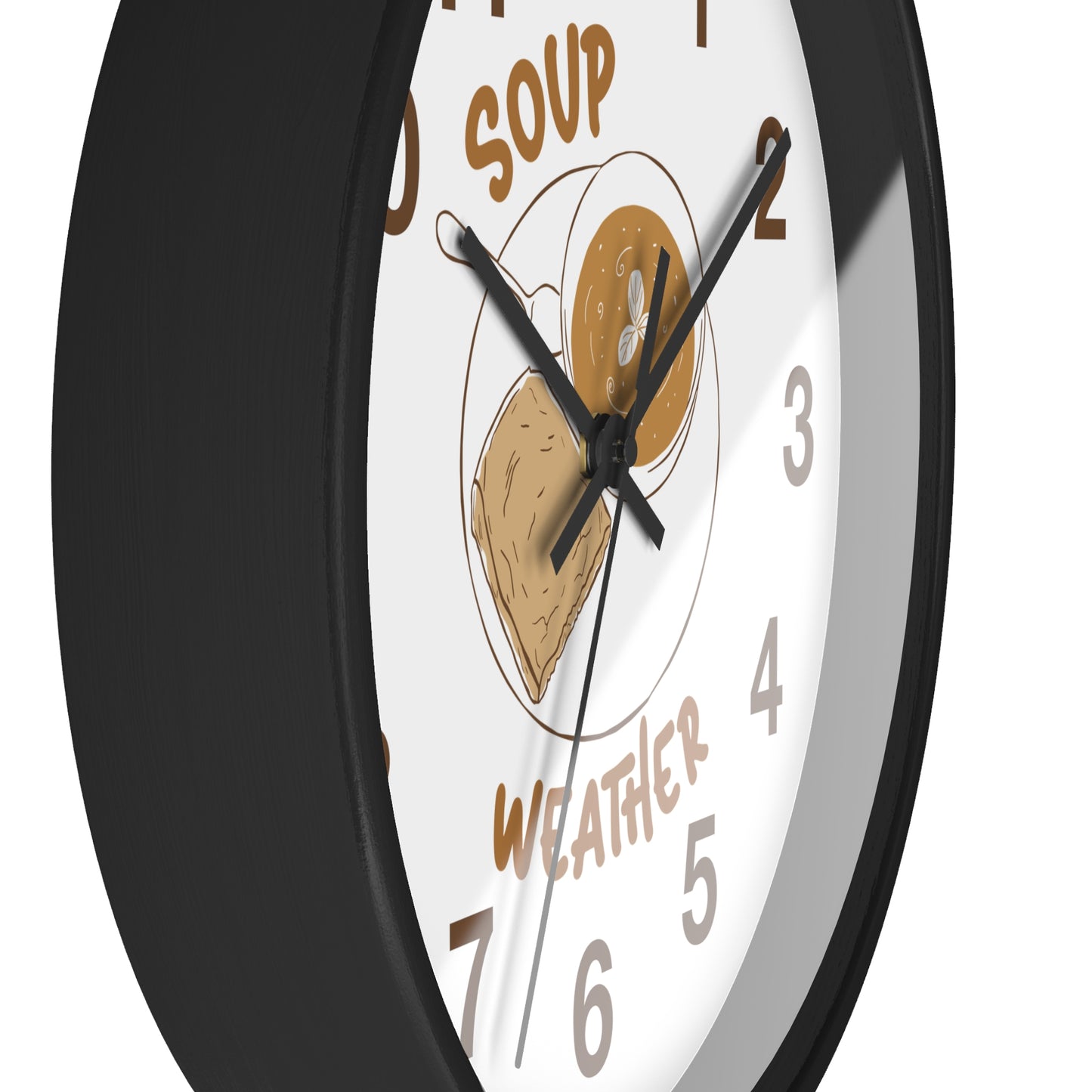 A close-up of a round wall clock with a black frame and a white face. The clock face features a food illustration in the center with the words 'SOUP' and 'WEATHER' in brown text, along with brown numerals.