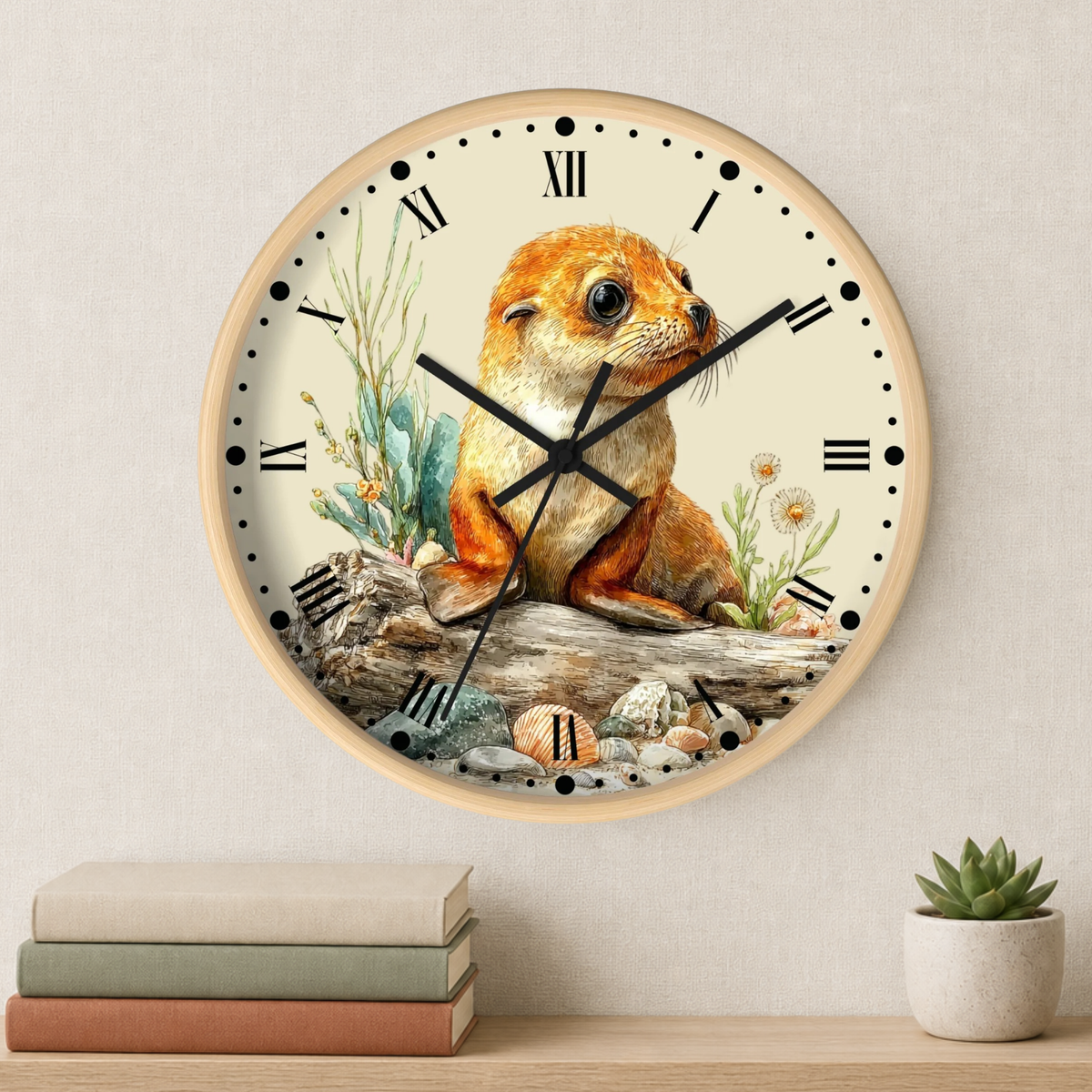A round wall clock with a light wood frame and a cream dial, featuring an illustration of a brown and cream seal pup sitting on a log with plants and shells. The clock is mounted on a textured beige wall above a shelf with books and a small potted succulent.