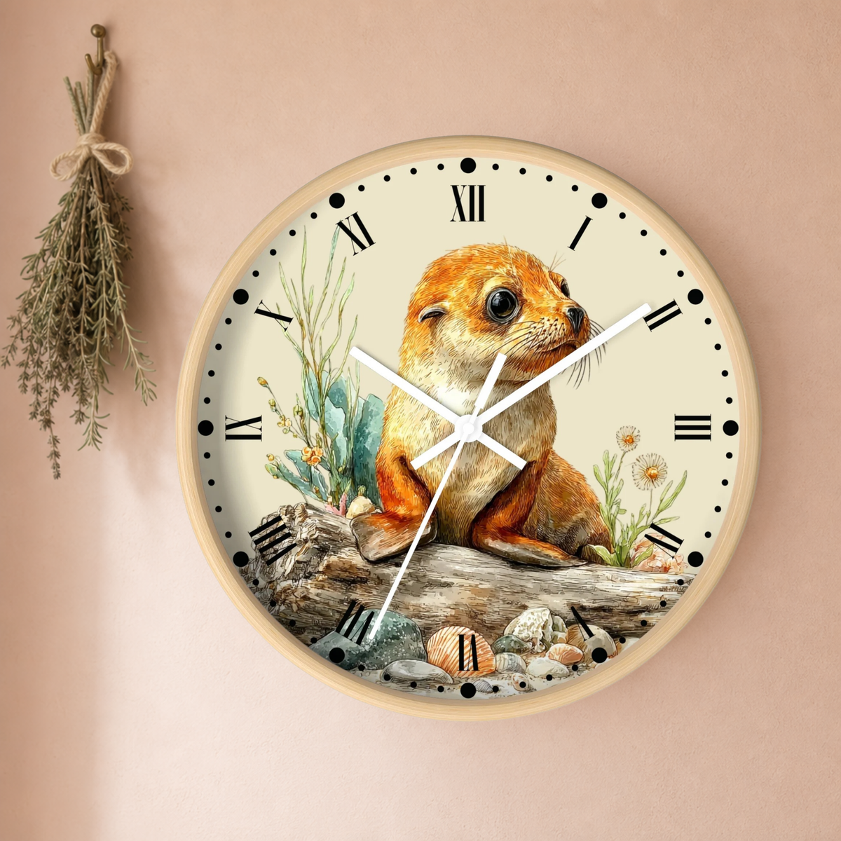 A round wall clock with a natural wood frame and a cream-colored face, featuring a detailed illustration of a brown seal pup sitting on a log with rocks and plants. The clock is mounted on a warm beige wall with a dried herb sprig hanging to the left.