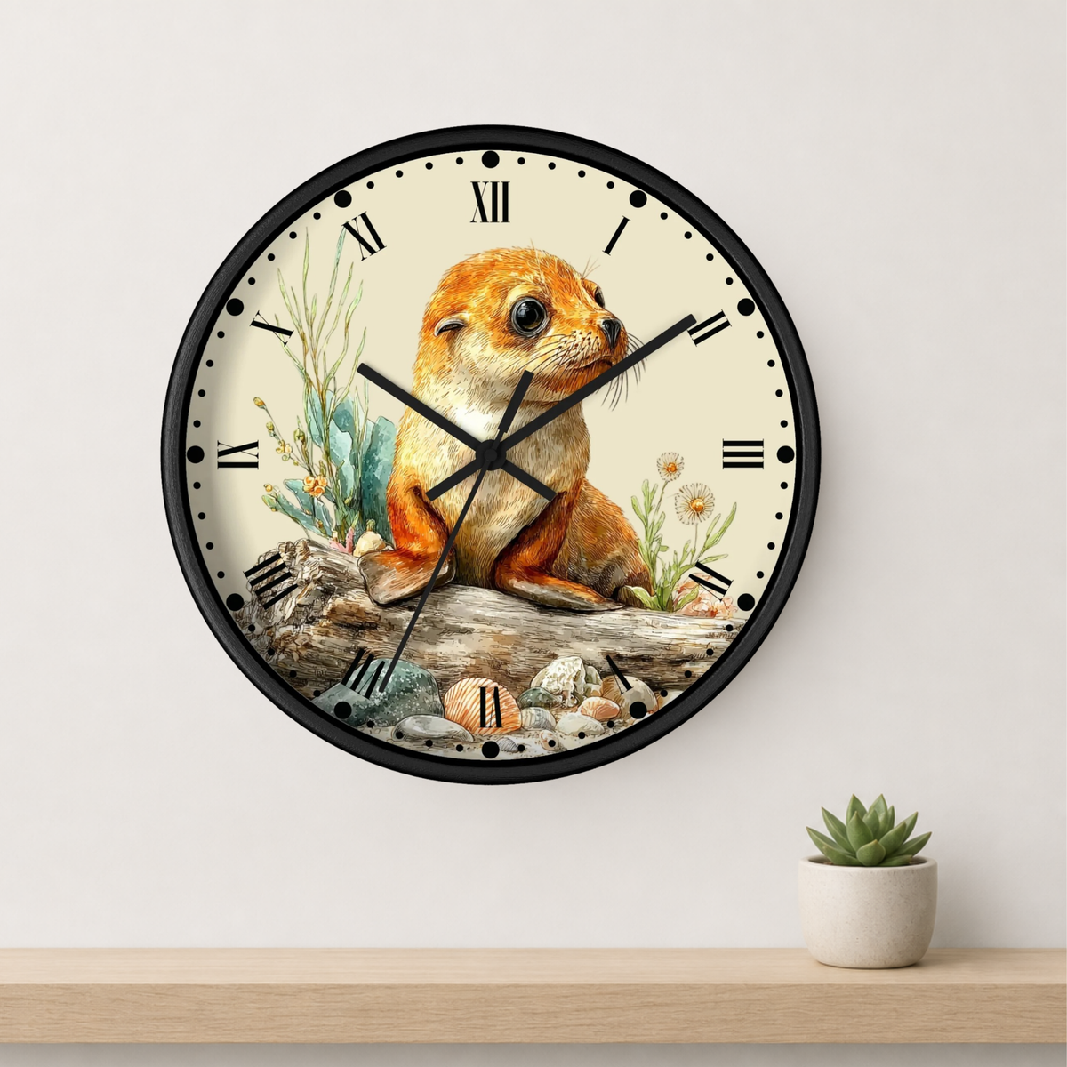 A round wall clock with a black frame and a cream-colored face featuring a detailed illustration of a seal pup sitting on a log with small plants. The clock is mounted on a light gray wall above a wooden shelf with a small potted succulent.