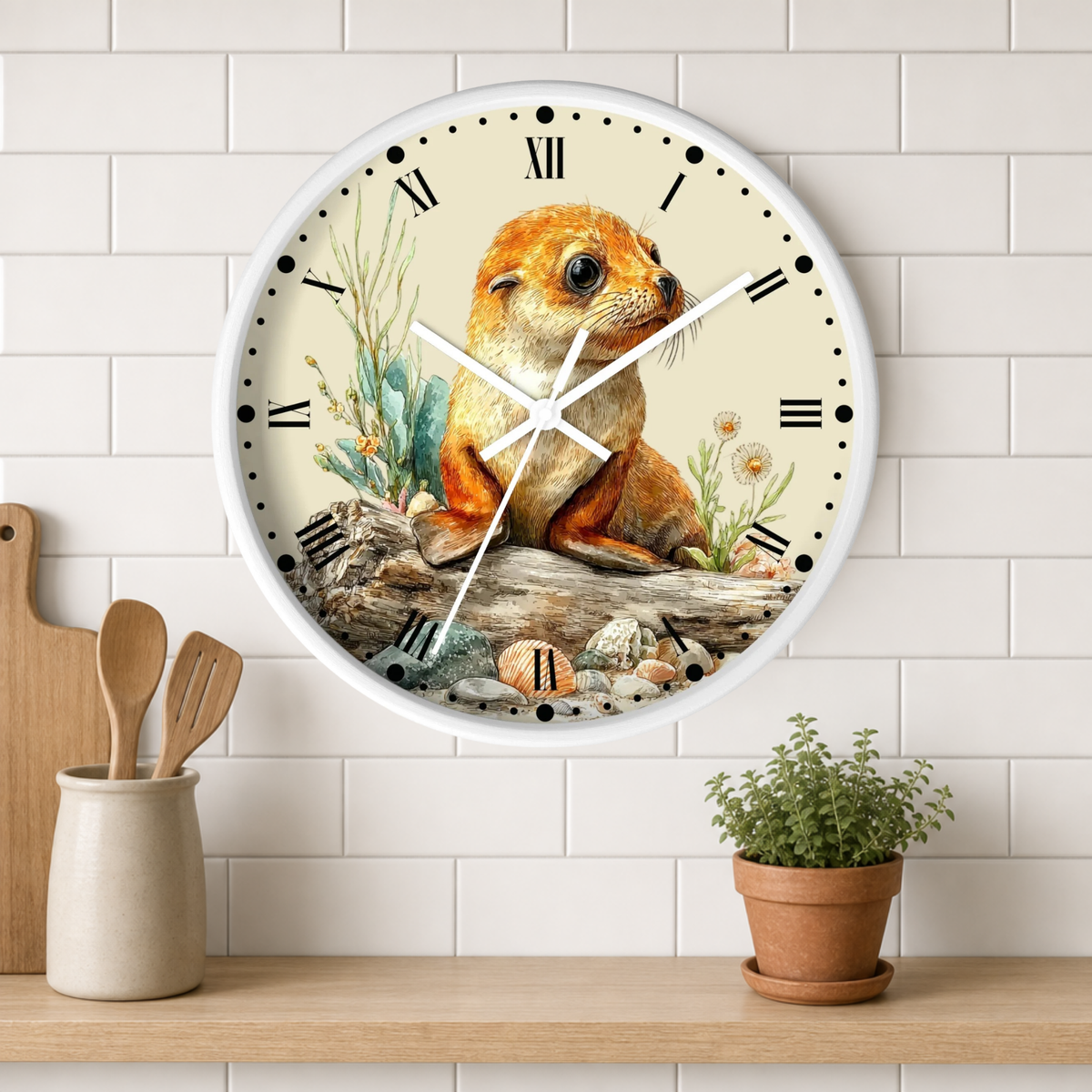 A round wall clock with a white frame and Roman numerals, featuring a detailed illustration of a seal pup sitting on a log with plants and rocks. The clock is mounted on a white subway tile wall above a wooden shelf with a small potted plant and wooden utensils.