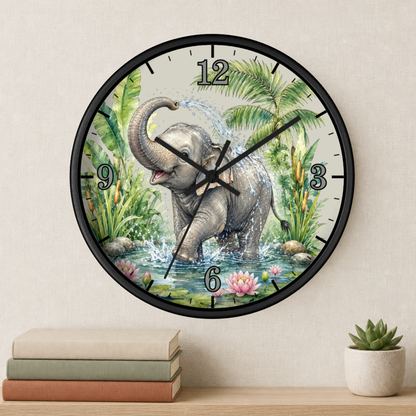 Round wall clock with a black frame and a printed illustration of a baby elephant standing in water among tropical plants. The clock is mounted on a beige wall above a wooden shelf with stacked books and a small potted succulent.