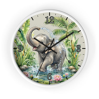 A round wall clock with a white frame and a printed illustration of a playful gray elephant standing in shallow water, surrounded by tropical green foliage, palm leaves, pink flowers, and black Arabic numerals on a light beige clock face.