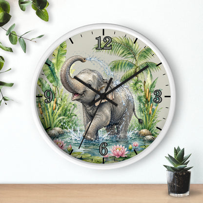 A round wall clock with a white frame and a printed illustration of a gray elephant standing in water among green tropical plants. The clock is mounted on a white wall above a light wood surface, with small green plants in the corners.