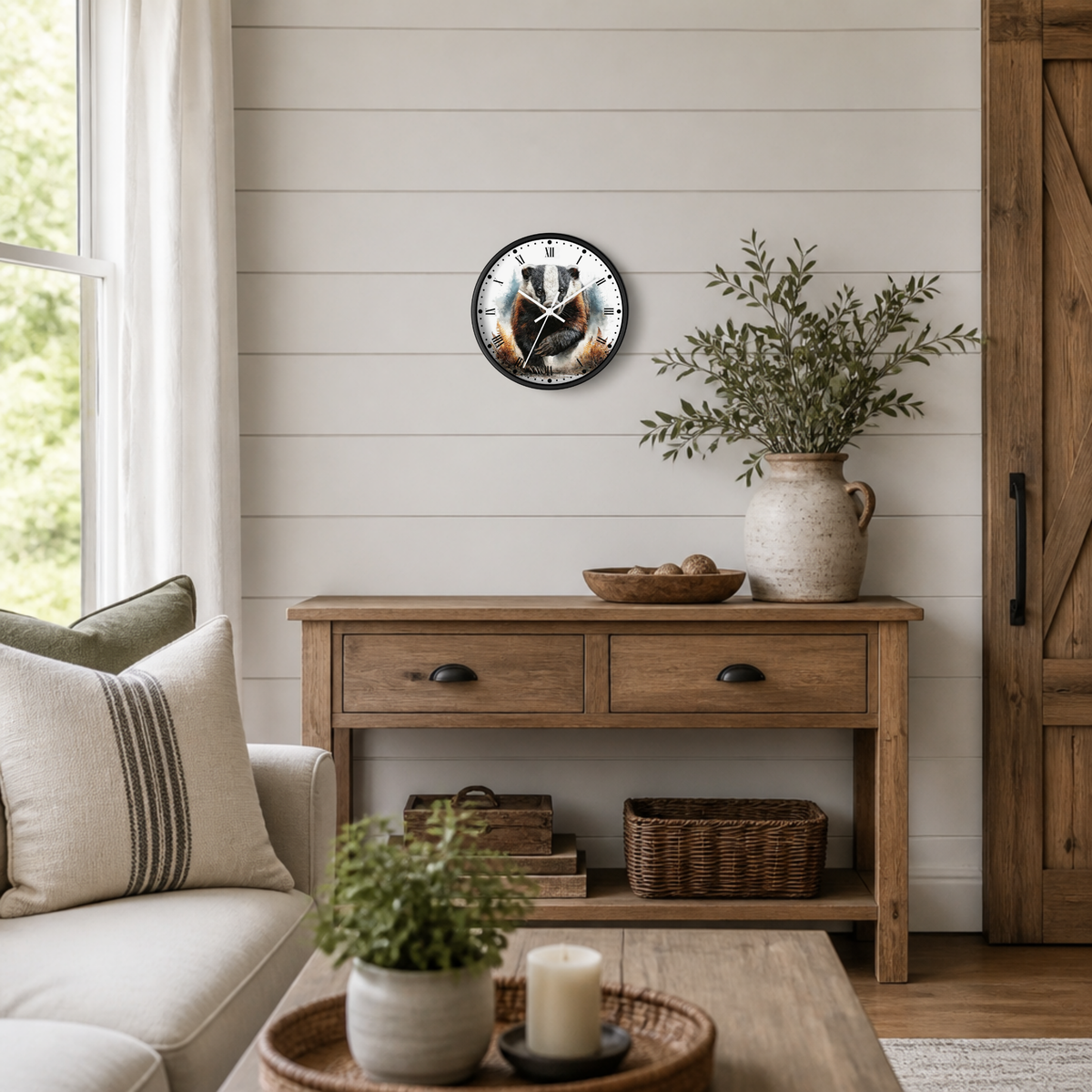 A round wall clock with a black frame and a rustic badger illustration, styled on a white shiplap wall above a wooden console table in a bright, modern farmhouse living room.