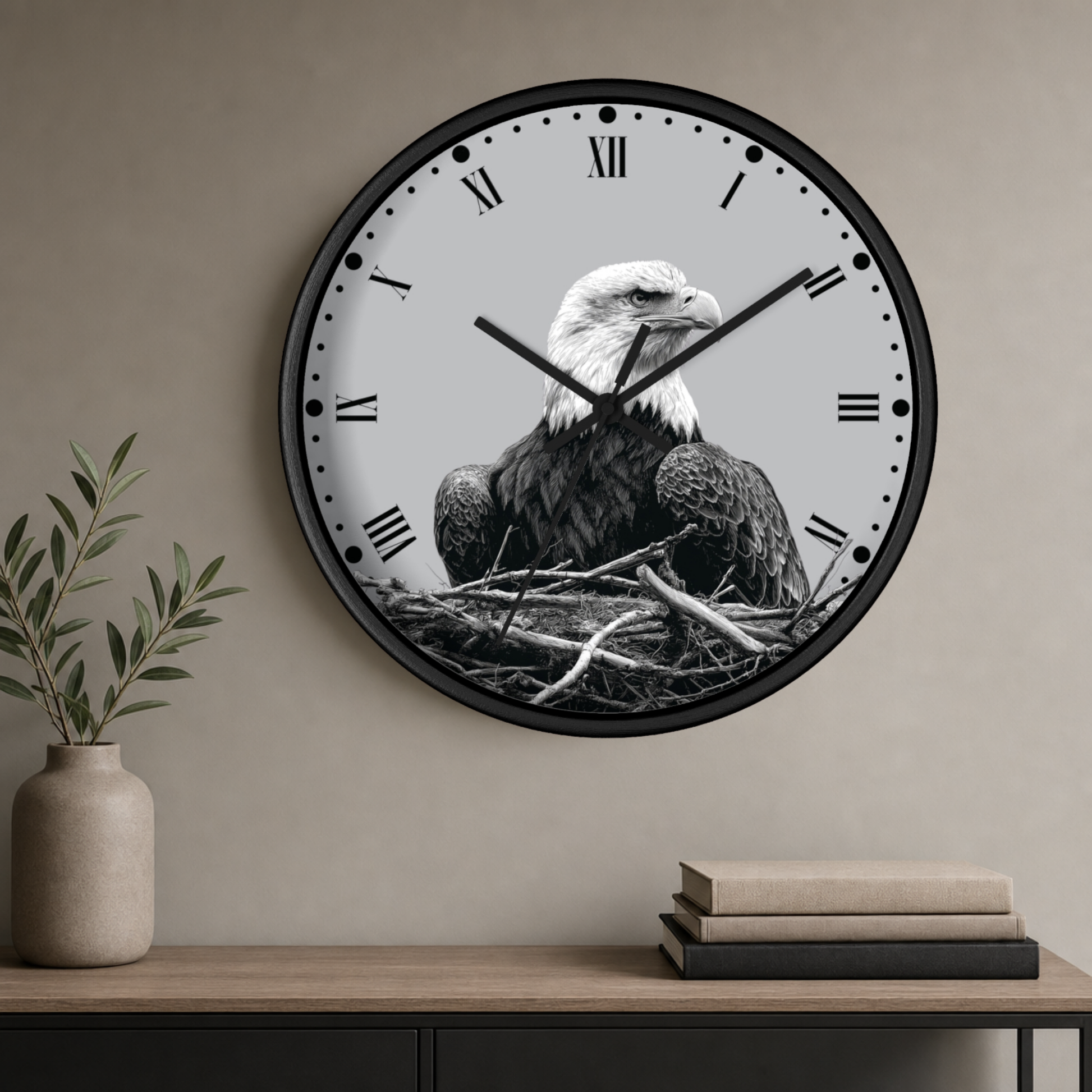 A large round wall clock with a black frame and a grayscale eagle sitting in a nest design on the face, mounted on a beige wall above a console table with a vase and books.