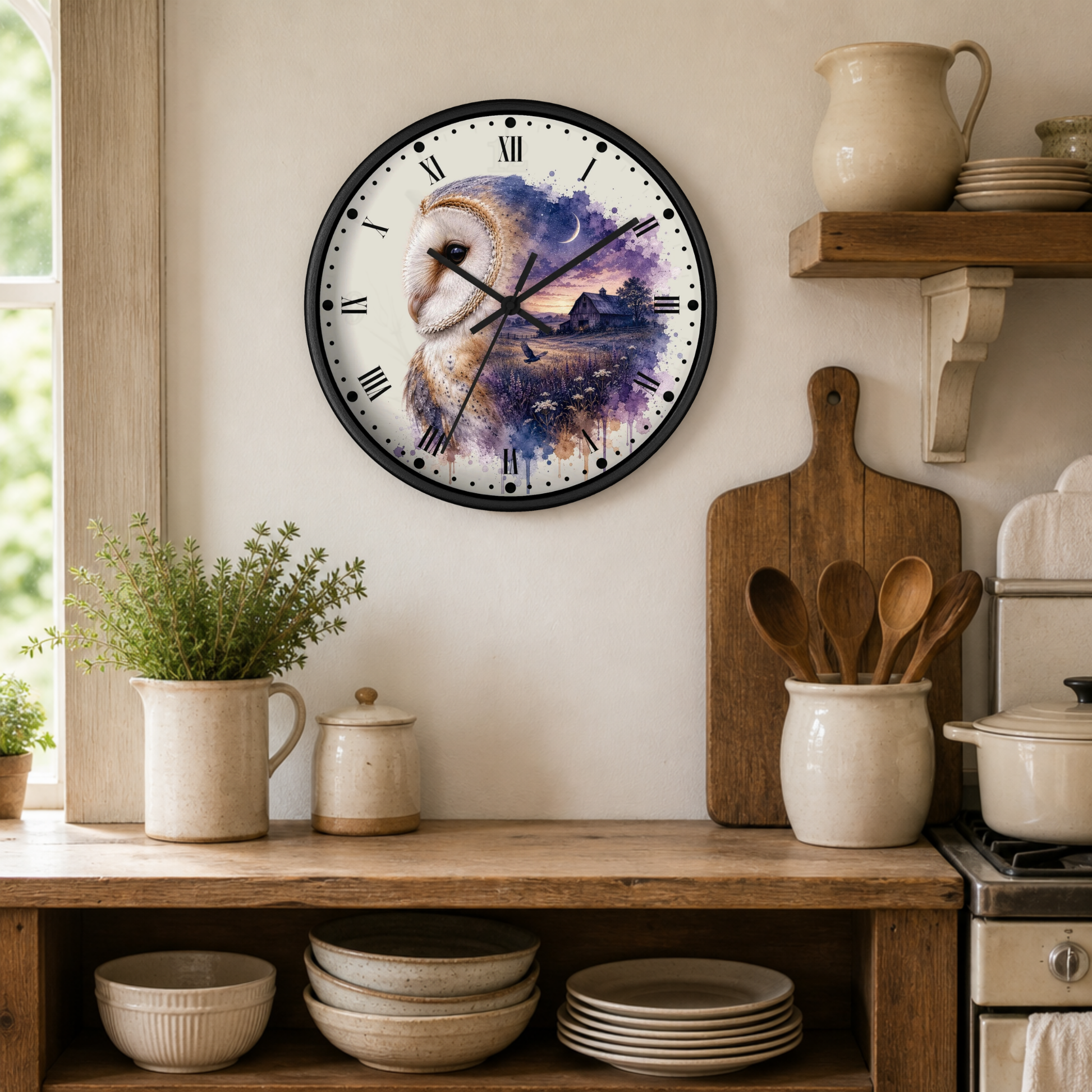 A round wall clock with a black frame and a watercolor-style owl landscape design on the face, mounted on a beige wall in a rustic kitchen setting with wooden shelves, ceramic dishes, and plants.